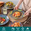A table setting with plates and bowls of food, a glass of water, and a person's hands holding a plate. Produktbild-Vorschau