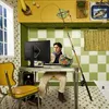 A person is sitting at a desk in a surreal kitchen setting, using a computer. Produktbild-Vorschau