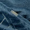 A close-up view of a textured blue fabric with a metallic grid pattern and a small gray tag with gold lettering. Produktbild-Vorschau