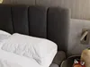 A close-up view of a bed with a dark gray upholstered headboard and white bedding. Produktbild-Vorschau