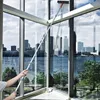 Person reinigt mit langem silbernem Teleskop-Fensterreiniger mit orangem Griff ein großes Glasfenster mit Blick auf Stadtsilhouette und Fluss Produktbild-Vorschau