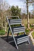 A three-tiered planter stand is shown outdoors in a garden setting. Produktbild-Vorschau