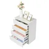 A white chest of drawers with several drawers open, revealing folded clothes and other items. A vase with flowers and two photo frames are on top. Náhľad obrázku produktu