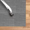 A close-up view of a chair leg with a roller on a grey textured mat, with a wooden floor visible on the right side. Podgląd zdjęcia produktu