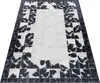 A rectangular rug with a patchwork design of black and white cowhide patterns, laid out on a white surface. Produktbild-Vorschau