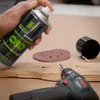 A hand holding a spray can of compressed air over a wooden surface with a drill and sandpaper. Produktbild-Vorschau