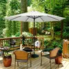 A patio umbrella and furniture set on a wooden deck surrounded by trees and greenery. Produktbild-Vorschau