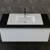 A close-up view of a white ceramic sink with a black countertop and a white cabinet underneath, set against a textured gray wall. Produktbild-Vorschau