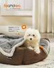 A small white dog is resting in a brown dog bed with a gray blanket. Produktbild-Vorschau