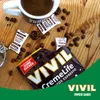 A close-up shot of VIVIL Creme Life Brasilitos Espresso candies and coffee beans scattered on a wooden surface, with a cup of coffee in the background. Produktbild-Vorschau