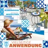A woman relaxing on a lounge chair on a balcony overlooking the sea, with mosaic tables and plants around her. Produktbild-Vorschau