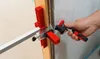 A person's hand is shown adjusting a tool that is clamping a door frame. Anteprima dell’immagine prodotto