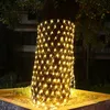 A tree trunk wrapped in a net of warm white lights at night. Náhľad obrázku produktu
