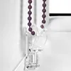 Close-up of a clear plastic bracket holding a purple beaded pull cord for a roller blind. Produktbild-Vorschau
