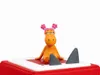 A small orange toy figure with pink hair is sitting on a red and white surface, with two gray shark fins sticking out of the surface. Produktbild-Vorschau