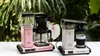 Two Moccacoffee makers are displayed on a white surface with a blurred green leafy background. Náhľad obrázku produktu