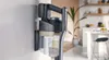 A cordless vacuum cleaner is mounted on a wall bracket in a kitchen setting. Náhľad obrázku produktu