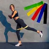 A woman is performing a leg exercise with a resistance band around her thighs, while other resistance bands are displayed in the background. Náhled obrázku produktu