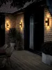 Outdoor patio at night with wall lights illuminating a brick wall and wooden deck. Produktbild-Vorschau
