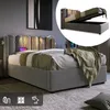 A grey upholstered bed with a tufted headboard is shown in a bedroom setting. A smaller inset image shows the bed frame lifted to reveal storage space underneath. Podgląd zdjęcia produktu