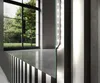 A close-up view of a modern mirror with integrated LED lighting, reflecting a room with large windows and greenery outside. Produktbild-Vorschau