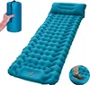 A teal-colored inflatable sleeping mat with a pillow, shown partially packed in a bag held by a hand, and a person's foot on the mat. Produktbild-Vorschau
