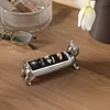 A silver cat-shaped ring holder is on a wooden desk, holding several rings. Glasses and a mesh container are in the background. Anteprima dell’immagine prodotto