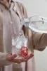 A person pouring sparkling water into a glass with ice and a slice of blood orange. Produktbild-Vorschau