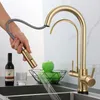 A hand is holding a gold kitchen faucet spray head, with water spraying out into a sink. A bottle of wine, a glass, and a bowl of green apples are on the counter. Podgląd zdjęcia produktu