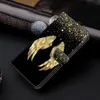 A black flip phone case with golden angel wings and glitter accents, placed on a dark surface. Produktbild-Vorschau