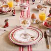 A Christmas-themed breakfast table setting with plates, cups, cutlery, orange juice, coffee, yogurt, and decorative Christmas figures. Voir les images du produit