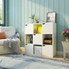 A white modular storage unit with nine compartments, some with doors and some open, filled with books, decorative items, and a storage box. It's placed in a room with light green paneled walls and a window with natural light. A portion of a white sofa with Voir les images du produit