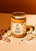 A jar of peanut butter is surrounded by peanuts and shells, with a warm, studio-like lighting. Produktbild-Vorschau