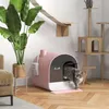A cat is exiting a pink litter box next to a large potted plant and a wooden cat tree. Produktbild-Vorschau