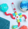 A colorful bath toy with pipes and a water bottle is laid out on a blue polka dot surface next to a blue towel and bath sponges. Produktbild-Vorschau