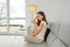 A woman is relaxing on a sofa with a back massager. Produktbild-Vorschau
