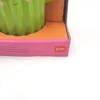 A close-up view of a green ceramic cactus pen holder inside its pink and orange packaging, with the brand logo visible. Voir les images du produit