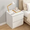 A white nightstand with a lamp, books, and a phone on top, next to a bed. Produktbild-Vorschau