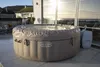 An inflatable hot tub is situated on a patio with a view of the ocean and houses in the background. Produktbild-Vorschau