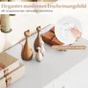 A close-up view of decorative cat figurines on a white surface, with a leather-bound notebook in the background. A circular inset shows a hand wiping a surface with a cloth, illustrating ease of cleaning. Produktbild-Vorschau