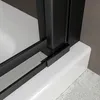 A close-up view of the corner of a black framed shower door resting on a white shower tray. Produktbild-Vorschau