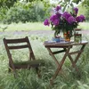 A table and chair set up outdoors in a grassy area with a bouquet of flowers and drinks on the table. Náhled obrázku produktu