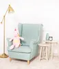 A plush unicorn sits on a mint green armchair next to a floor lamp and small side tables. Produktbild-Vorschau