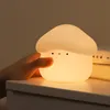 A hand is touching a mushroom-shaped night light on a white surface, with books in the background. Podgląd zdjęcia produktu