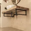 A bathroom sink with a wooden countertop and black metal brackets, showing plumbing underneath. Produktbild-Vorschau
