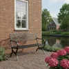 A black metal garden bench sits on a brick patio next to a brick building, with a canal and houses in the background. Anteprima dell’immagine prodotto