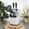 A kitchen utensil holder with various utensils inside, placed on a wooden surface with plants in the background. Produktbild-Vorschau