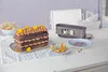 A chocolate cake with frosting and yellow flowers, along with baking accessories and ingredients, is displayed on a table. Anteprima dell’immagine prodotto