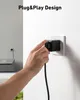 A hand is plugging a black device into a white electrical outlet on a white wall. Another electrical outlet with a device plugged in is visible on the left side of the image, along with a gray electronic device. Produktbild-Vorschau