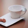 A white coffee cup and saucer with two cookies on a table. Produktbild-Vorschau